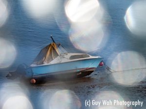 A picture of a boat on the shore at Shoreham beach, taken through broken glass, creating a bokeh effect